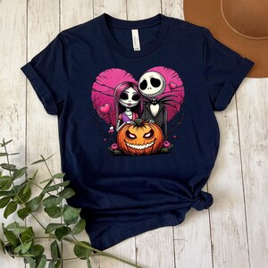 Puede incluir: Camiseta azul marino con una ilustraci&oacute;n de dibujos animados de Jack Skellington y Sally de Pesadilla antes de Navidad, con un fondo de coraz&oacute;n rosa y una calabaza. El dise&ntilde;o est&aacute; centrado en la camiseta.