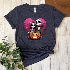 Puede incluir: Camiseta gris oscuro con un dise&ntilde;o tem&aacute;tico de Halloween. El dise&ntilde;o incluye un coraz&oacute;n rosa, una calabaza sonriente y personajes estilizados. La camiseta est&aacute; hecha de un material suave y tiene un cuello redondo cl&aacute;sico.