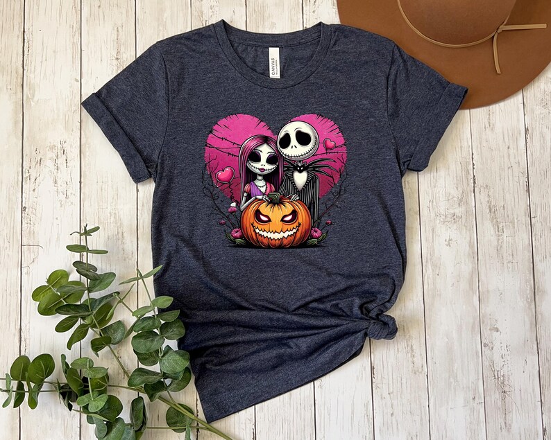 Puede incluir: Camiseta gris oscuro con un dise&ntilde;o tem&aacute;tico de Halloween. El dise&ntilde;o incluye un coraz&oacute;n rosa, una calabaza sonriente y personajes estilizados. La camiseta est&aacute; hecha de un material suave y tiene un cuello redondo cl&aacute;sico.