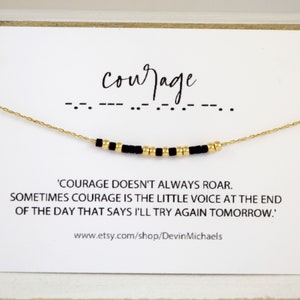 May include: A gold-colored chain necklace with black and gold beads spelling out "courage" in Morse code. The necklace is displayed on a white card with the text: "Courage doesn't always roar..." and the Etsy shop URL.
