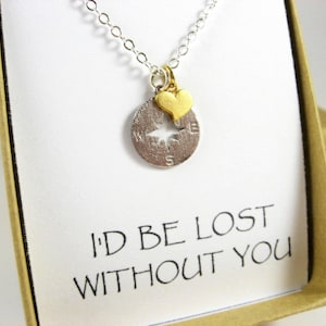 May include: A silver necklace with a compass charm and a gold heart charm. The necklace is in a box with a white card that says "I'd be lost without you".