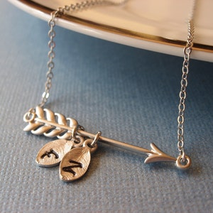 May include: Silver necklace with an arrow pendant and two leaf charms with the letters "E" and "N" engraved on them.