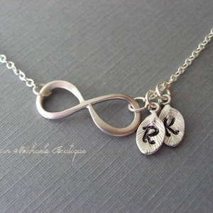 May include: Silver infinity necklace with two small leaf charms, each with a letter, 'R' and 'K', engraved on them.