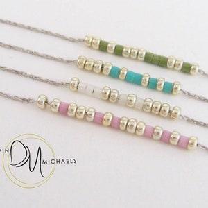 May include: Four delicate necklaces with silver chains and colorful beaded accents. The beads are in shades of green, turquoise, white, and pink. The necklaces are displayed on a white background. The brand logo "Devin Michaels" is in the lower left corner.