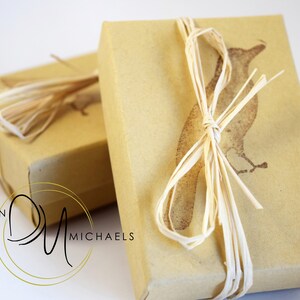 May include: Two brown gift boxes tied with natural twine. The top box has a brown bird illustration and the text "Devin Michaels".