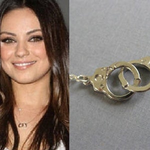 May include: A silver necklace with a handcuff pendant. The necklace is worn by a woman with long brown hair.