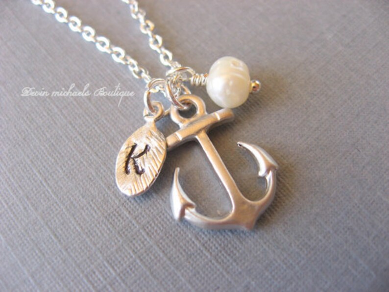 May include: A silver anchor necklace with a small pearl charm and a silver charm with the letter K engraved on it.
