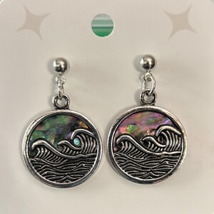 May include: A pair of silver-toned dangle earrings. Each earring features a circular pendant with a wave design and iridescent abalone shell inlay. The earrings have a post and chain attachment.