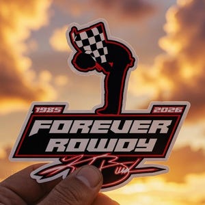 Pode incluir: Um autocolante com as palavras "FOREVER ROWDY" em branco e vermelho, com os anos 1985 e 2026. O autocolante apresenta uma silhueta preta de uma pessoa segurando uma bandeira quadriculada. O fundo é um pôr do sol.