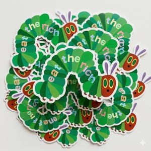 Könnte beinhalten: Eine Ansammlung grüner und roter Raupenaufkleber mit dem Text "eat the rich" in Regenbogenfarben. Die Aufkleber zeigen ein Cartoon-Raupendesign mit rotem Gesicht, großen Augen und lila Antennen.
