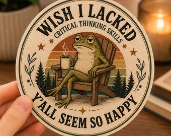 Pode incluir: Um adesivo redondo com um sapo verde sentado numa cadeira de madeira, segurando uma caneca de café. O texto diz WISH I LACKED CRITICAL THINKING SKILLS Y'ALL SEEM SO HAPPY. O design mostra um pôr do sol, pinheiros e estrelas em estilo vintage.