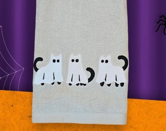 May include: A white kitchen towel with three embroidered ghost cats in black. The cats are in a row, facing forward, with their tails curled behind them.