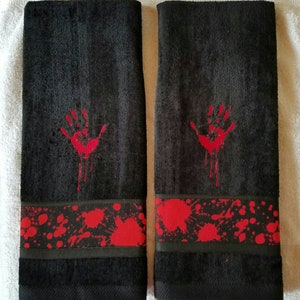 May include: Two black hand towels with a red handprint and blood splatter design. The towels have a red and black trim.