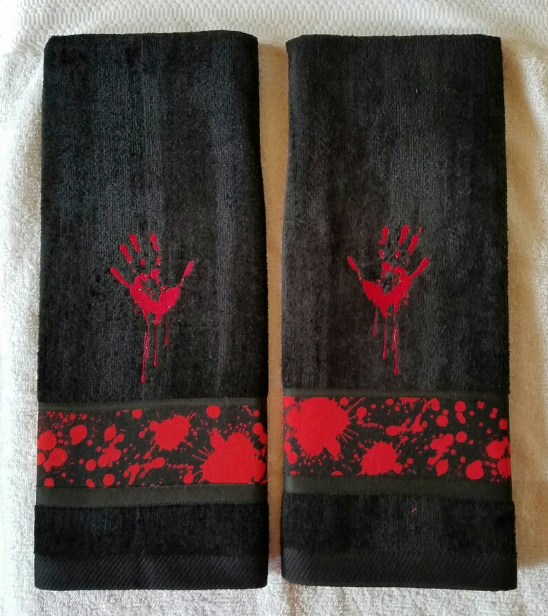 May include: Two black hand towels with a red handprint and blood splatter design. The towels have a red and black trim.