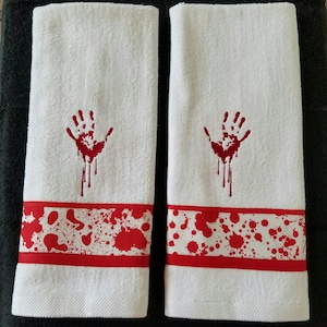 May include: Two white hand towels with red embroidered bloody handprints and red and white bloody splatter designs.