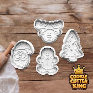 May include: Four white plastic Christmas cookie cutters: Santa Claus, a reindeer, a gingerbread man, and a Christmas tree. The cutters are on a wooden surface, with a rolling pin in the background. The Cookie Cutter King logo is in the bottom right corner.