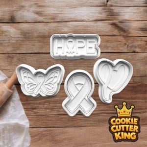 May include: A collection of white plastic cookie cutters. The shapes include a butterfly, a ribbon, a heart with a ribbon, and a rectangle with the word "HOPE". They are displayed on a wooden surface. The Cookie Cutter King logo is visible in the bottom right corner.