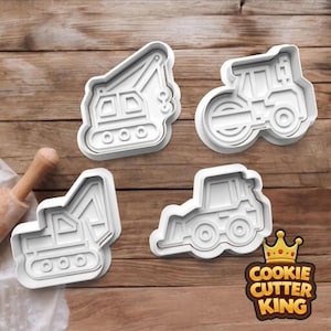 May include: Four white plastic cookie cutters shaped like construction vehicles: a crane, a road roller, an excavator, and a tractor. The Cookie Cutter King logo is in the bottom right corner. The cutters are on a wooden surface.