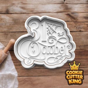 May include: A white plastic cookie cutter featuring the words "31 October" with a spider web and spider design. The cutter sits on a wooden surface, with a rolling pin and cloth visible. The Cookie Cutter King logo is in the bottom right corner.