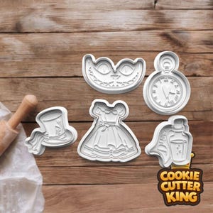May include: A selection of white plastic cookie cutters. The shapes include a Cheshire Cat grin, a pocket watch, a dress, a top hat, and a potion bottle. The cutters are displayed on a wooden surface.