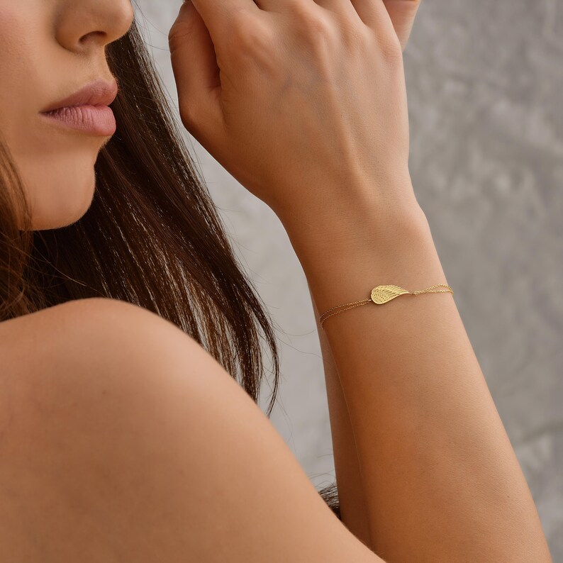 Pode incluir: Uma delicada pulseira dourada com um berloque em forma de folha. O berloque tem detalhes intrincados, e a pulseira &eacute; presa com uma corrente fina. A joia &eacute; usada no pulso, mostrando seu design elegante.