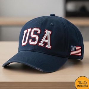 May include: Navy blue baseball cap with the word "USA" in white letters with red trim. An American flag patch is on the side. The cap is made of a durable fabric and has a curved brim.