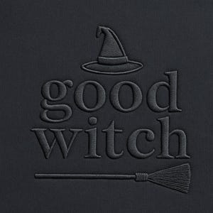 May include: Black fabric featuring embroidered text and a witch hat and broom design. The words "good witch" are embroidered in a stylized font. The witch hat is above the word "good" and the broom is below the word "witch".