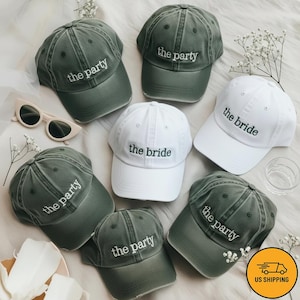 May include: Several baseball caps in faded green and white. The green caps are embroidered with "the party", while the white ones say "the bride". The caps are displayed on a light-coloured surface, with a pair of sunglasses visible.