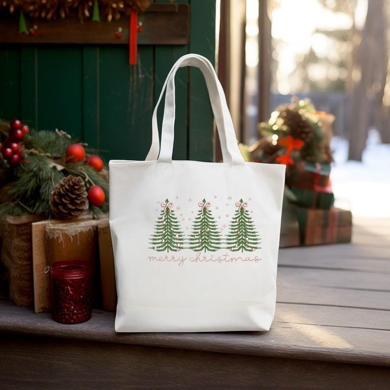 May include: A white tote bag featuring three green Christmas trees with pink bows and the words "merry christmas" in a pink script. The bag has two white handles and is made of a sturdy material.