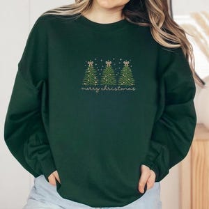 May include: Dark green sweatshirt with embroidered Christmas trees and the text "merry christmas" in a delicate script. The trees are decorated with tiny lights and bows, creating a festive holiday design.