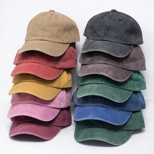 Puede incluir: Apilados gorras de béisbol en varios colores: beige, rojo, amarillo, rosa y burdeos a la izquierda, y carbón, marrón, verde, azul y turquesa a la derecha. Cada gorra tiene una visera curva y un botón superior.