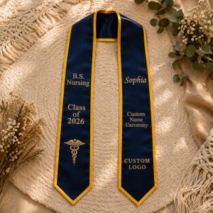 May include: A navy blue graduation sash with gold trim. The sash is personalized with the text "B.S. Nursing", "Class of 2026", a medical symbol, the name "Sophia", and "Custom Name University" and "CUSTOM LOGO".