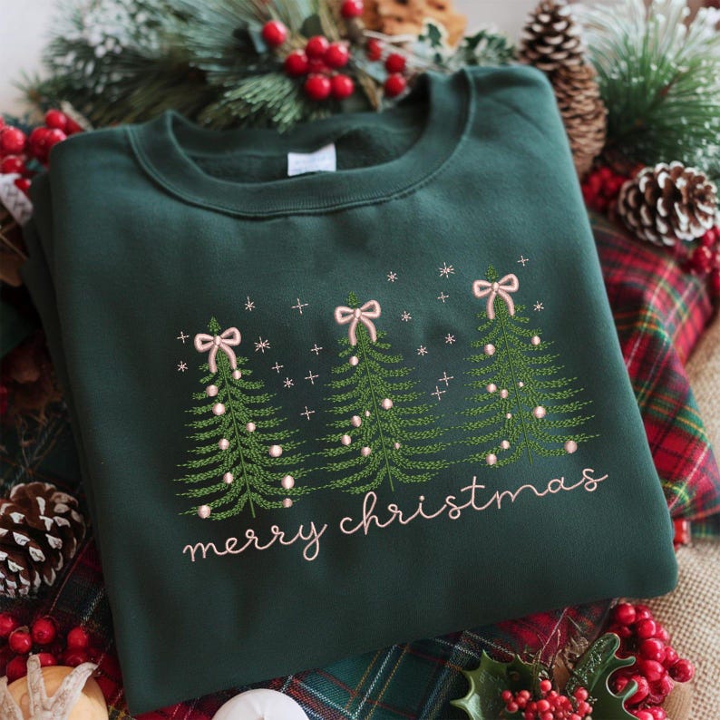 May include: A dark green sweatshirt with embroidered Christmas trees, bows, and the words "merry christmas" in a cursive font. The trees have white lights and pink bows. Festive holiday apparel.