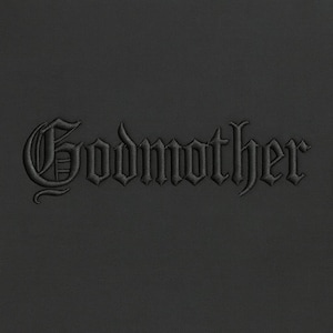 Puede incluir: Texto negro bordado sobre un fondo negro texturizado. El texto dice "Godmother" en una fuente gótica. La imagen es un primer plano, centrado en la palabra bordada.