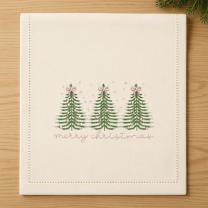 May include: Cream-colored Christmas table runner with embroidered green Christmas trees, pink bows, and the words "merry christmas" in pink. The runner has a dotted border.