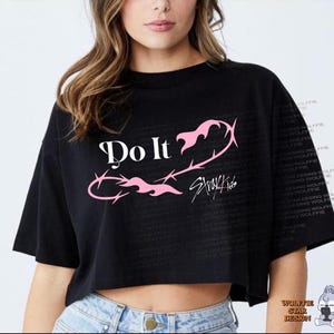 Puede incluir: Camiseta corta negra con las palabras "Do It" en blanco y un diseño gráfico rosa. El texto "Stray Kids" está debajo del gráfico. La camiseta tiene mangas cortas y cuello redondo.