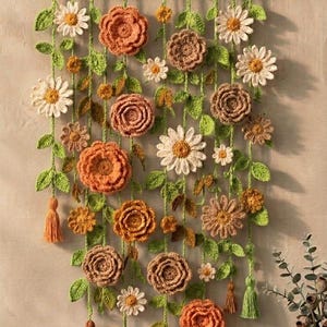 May include: A wall hanging featuring crocheted flowers in shades of orange, brown, and white, with green crocheted leaves and vines suspended from a horizontal wooden dowel. The arrangement includes various floral shapes and small hanging tassels.