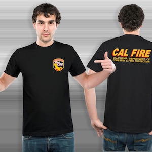 Pode incluir: T-shirts pretas com o logotipo "CAL FIRE" na frente e atrás. O logotipo da frente é um escudo com as palavras "CAL FIRE" e um gráfico de uma chama. A parte de trás da camisa tem as palavras "CAL FIRE" e "CALIFORNIA DEPARTMENT OF FORESTRY & FIRE PROTECTION".
