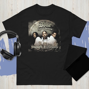 May include: Black t-shirt featuring a graphic of the hip-hop group Bone Thugs-n-Harmony. The graphic includes the group's name, members' images, and the words "Strength & Loyalty". The shirt is made of a soft material.