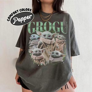 Puede incluir: Camiseta gris oscuro con un gr&aacute;fico de Grogu de The Mandalorian. La palabra "GROGU" est&aacute; impresa en verde encima de la imagen de Grogu. La camiseta tambi&eacute;n tiene las palabras "COMFORT COLORS" y "Pepper".