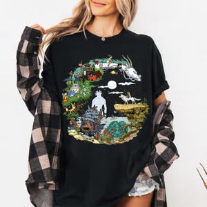 May include: Black t-shirt with a vibrant graphic depicting characters and scenes from an animated film. The design includes a white dragon, a girl, and other animated figures. The t-shirt is a comfortable, casual style.