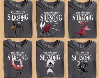 May include: Six gray t-shirts featuring the text "HOLLOW KNIGHT SILKSONG" in white. Each shirt displays a different character illustration in various colors, including red, black, and gold. The shirts are laid out on a wooden surface.