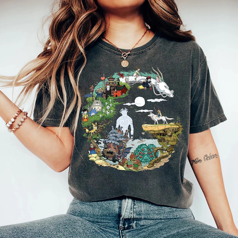 May include: Dark grey t-shirt with a vibrant illustration of animated characters and scenes. The design includes a white dragon, a castle, and other fantasy elements. The shirt is a crew neck and has a vintage wash.