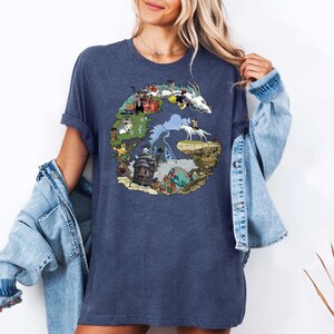 May include: A navy blue t-shirt featuring a colorful graphic design. The design is a stylized letter "G" filled with illustrations of characters and scenes from an animated film. The shirt is made of a soft material.