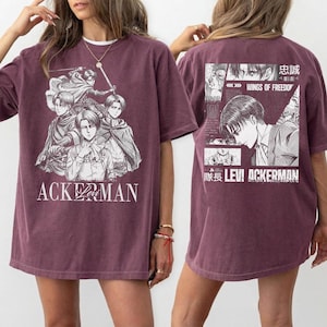 May include: Maroon t-shirt featuring a manga-style illustration of characters with the text "ACKERMAN" on the front. The back of the shirt displays a collage of images and text, including "WINGS OF FREEDOM" and "LEVI ACKERMAN".