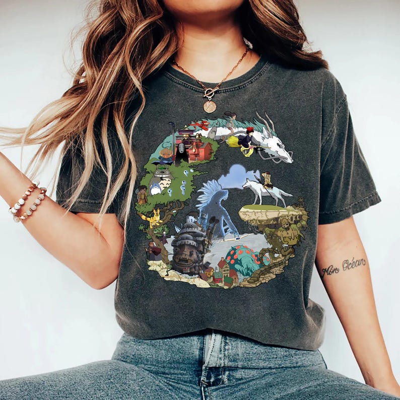 May include: Dark gray t-shirt featuring a colorful illustration of a dragon, characters, and landscapes. The graphic design is circular and includes a white dragon, a wolf, and various buildings. The shirt is a crew neck and has a vintage look.