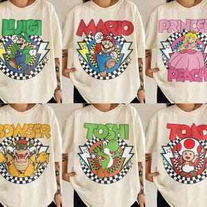 May include: A collection of six off-white t-shirts featuring graphic prints of Nintendo characters including Luigi, Mario, Princess Peach, Bowser, Yoshi, and Toad. Each shirt displays the character name, a checkered circle, and lightning bolts.