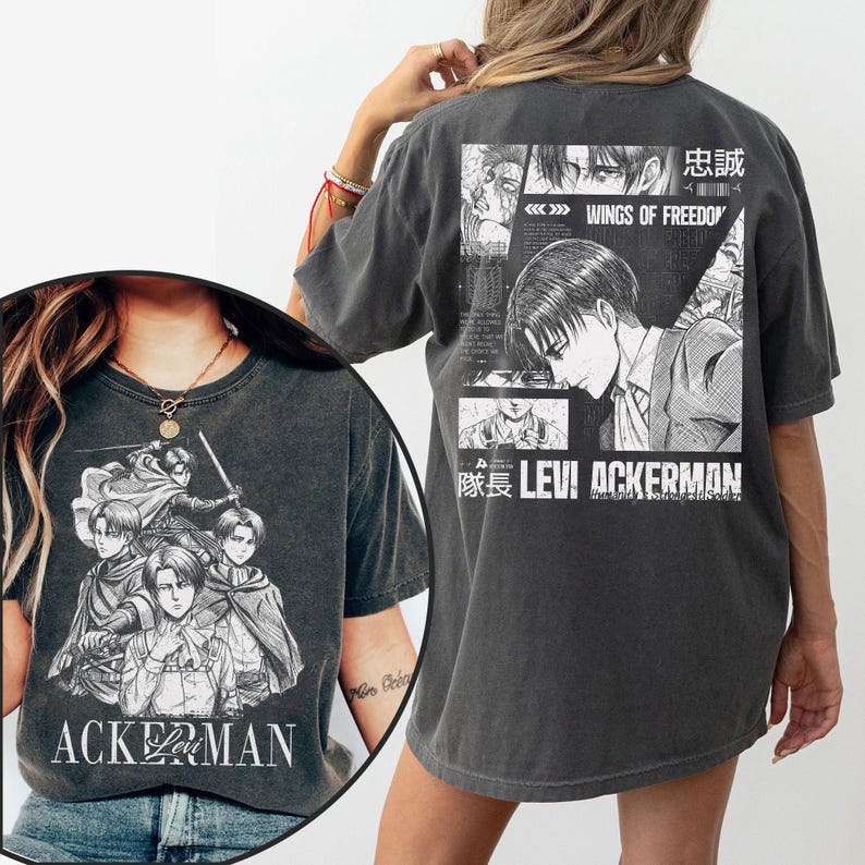 May include: Dark gray t-shirt featuring manga-style illustrations of characters. The front displays a group of figures with the text "ACKERMAN". The back has a larger graphic with the text "WINGS OF FREEDOM" and "LEVI ACKERMAN".