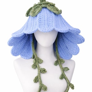 May include: A light blue crochet flower hat with green detailing. The hat is designed to resemble a large flower with multiple petal layers. Green leaves and a stem are at the top, with green vines and leaves hanging down.