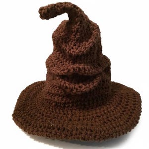 May include: A brown, crocheted hat with a wide brim and a pointed top. The hat is made of a textured yarn and has a slightly curved tip. The hat is a solid brown color and is likely a costume piece.